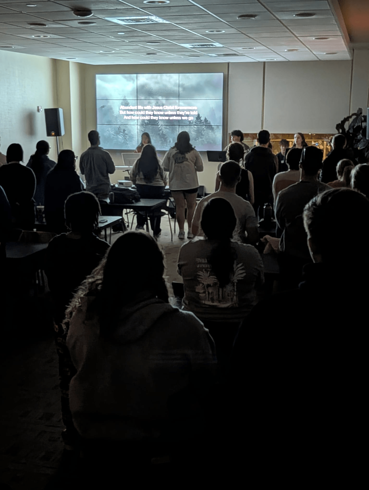 Students standing during worship with lyrics projected on screen